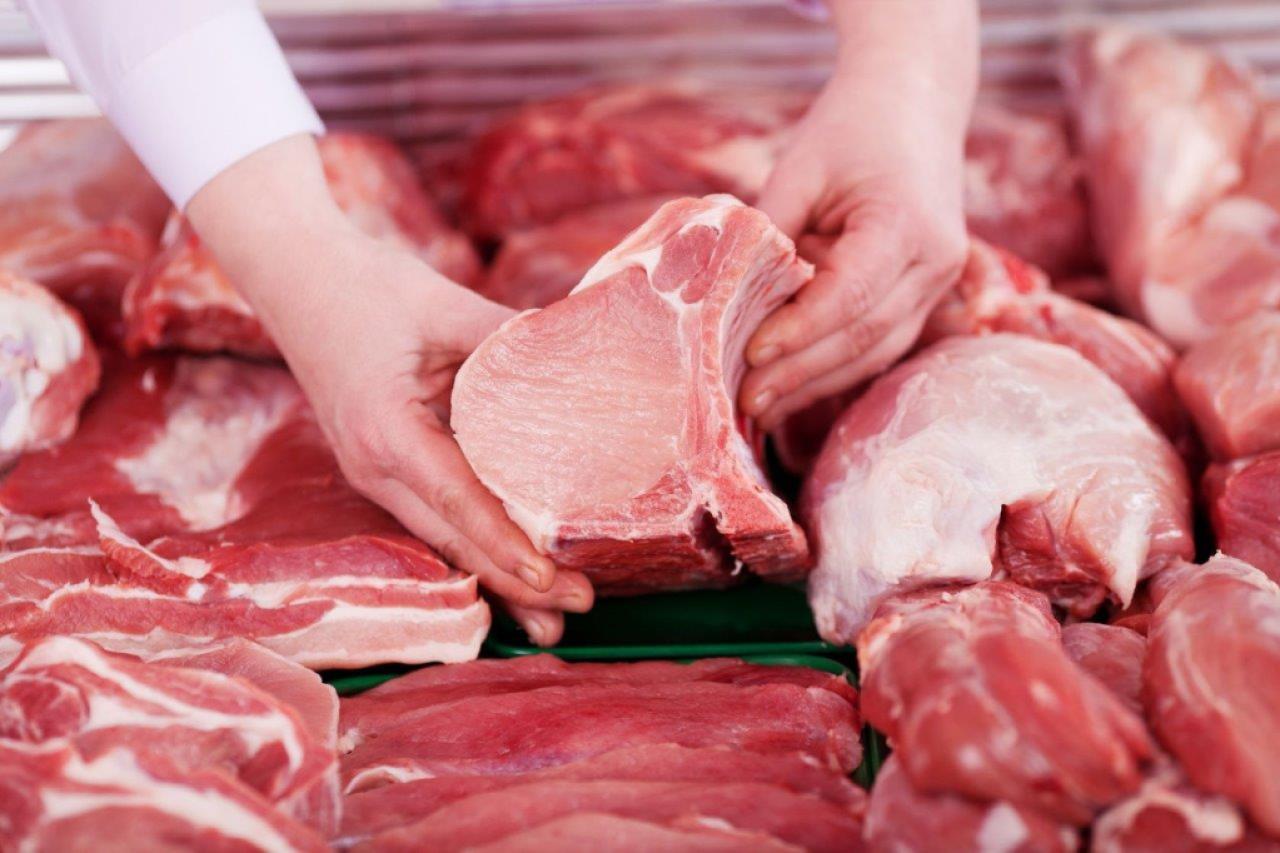 Hands picking up a fresh cut of pork. 